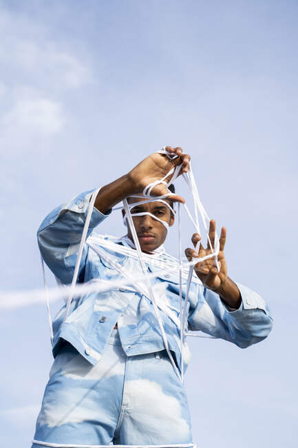 Eingeklemmter junger Mann entfernt Seil im Stehen gegen Himmel — Stockfoto