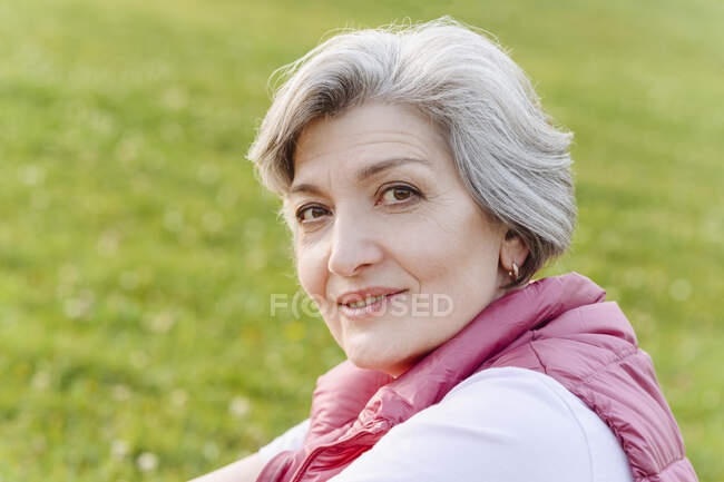 Mujer madura sonriente con el pelo gris en el parque público - foto de stock