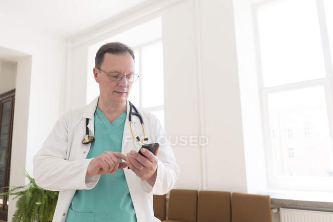 Doctor usando smartphone en corredor - foto de stock