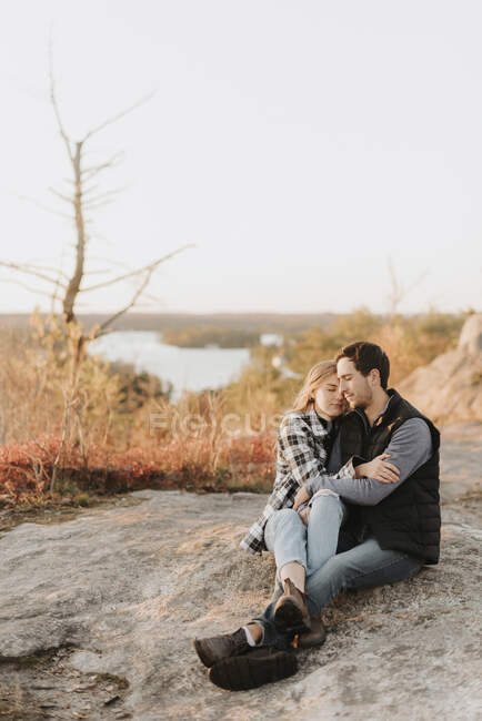 Young couple embracing on rocky surface during autumn hike - foto de stock