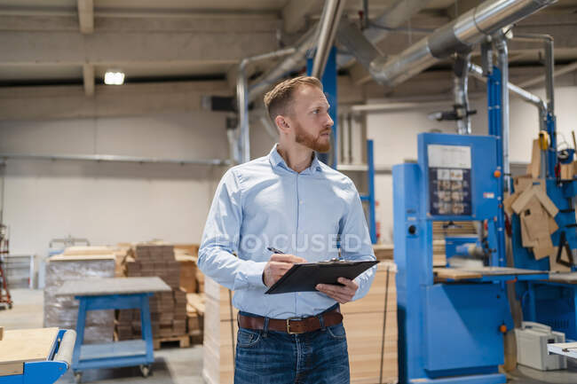 Portrait of carpenter standing in production hall with clipboard in hands - foto de stock