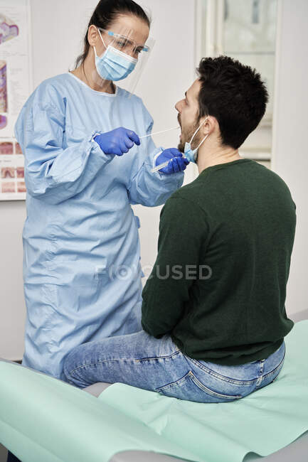 Médica recolhendo amostra da boca de paciente do sexo masculino para o teste COVID-19 — Fotografia de Stock