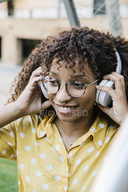 Donna sorridente che indossa cuffie ascoltare musica mentre in piedi all'aperto — Foto stock