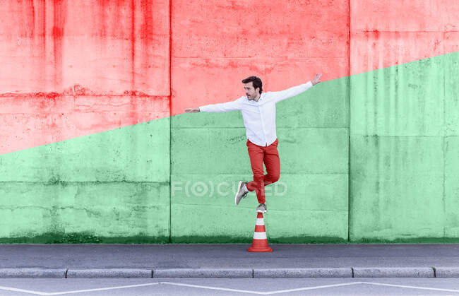 Carefree man standing on traffic cone against multi colored wall — Stock Photo