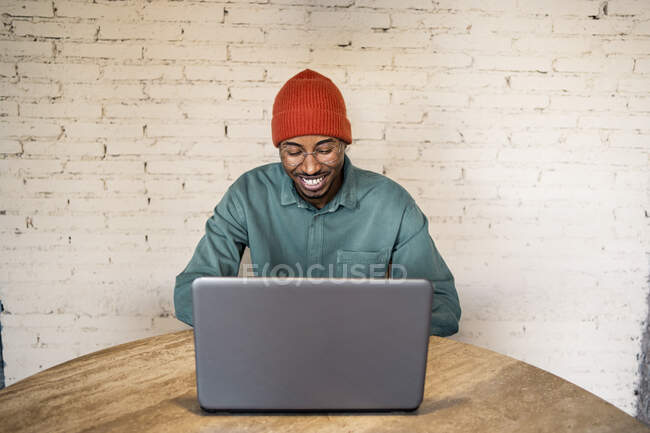 Щасливий чоловік, який використовує лептоп на столі проти білої цегляної стіни. — стокове фото