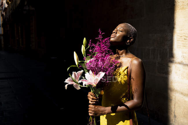 Hipster femenino con los ojos cerrados sosteniendo ramo de flores en el día soleado - foto de stock