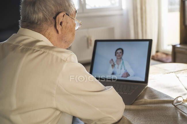 Uomo anziano che prende consigli dal medico femminile in video attraverso il computer portatile in soggiorno — Foto stock