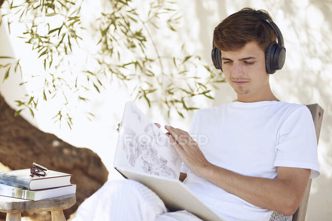 Junger Mann liest Buch und hört Musik gegen Wand — Stockfoto