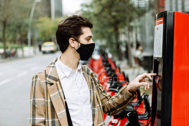 Hombre joven en la cara de la máscara de alquiler de bicicletas en la ciudad - foto de stock
