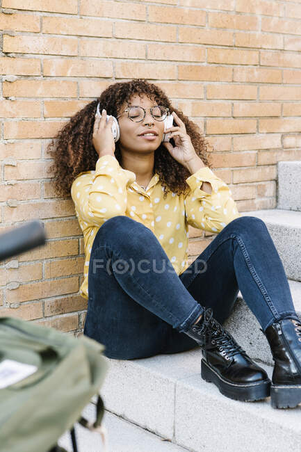 Junge Frau hört Musik, während sie auf Stufen sitzt — Stockfoto