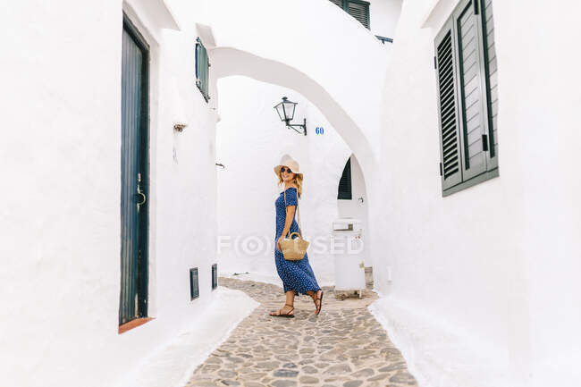 Женщина в шляпе ходит по аллее среди домов в деревне Бинибека, Минорка, Испания — стоковое фото