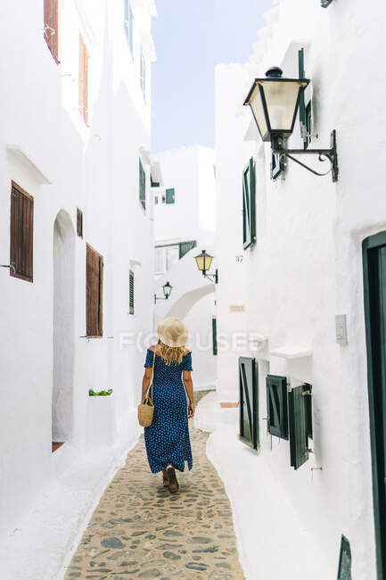 Mature woman wearing hat walking in alley amidst houses at Binibeca village, Minorca, Spain — Stock Photo