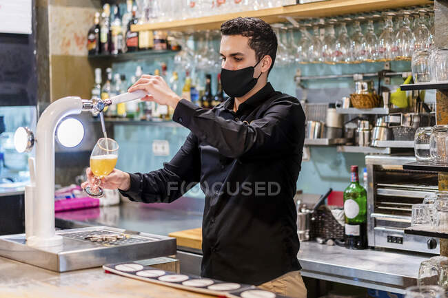 Портрет бармена в защитной маске, подающего пиво — стоковое фото