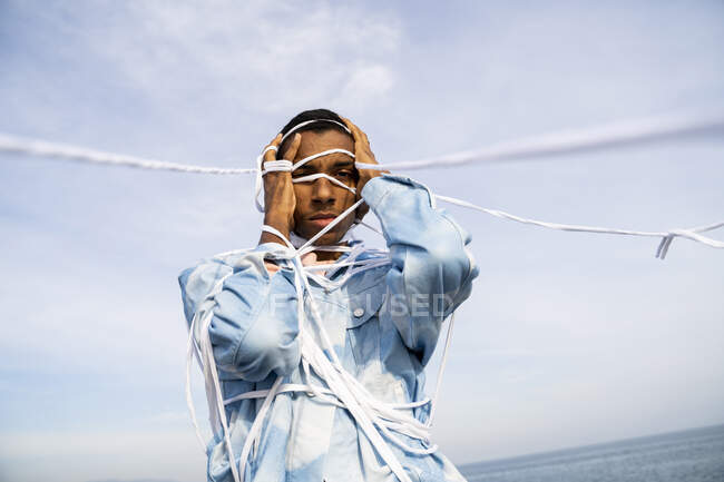 Man wrapped in rope standing with head in hands against sk — Stock Photo