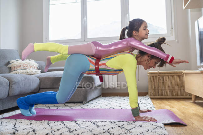 Mutter trägt Tochter beim Sport im heimischen Wohnzimmer auf dem Rücken — Stockfoto