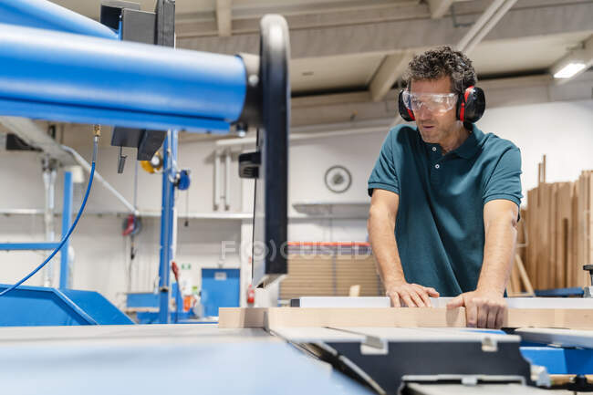 Carpenter cutting plank on circular saw in production hall — Stock Photo
