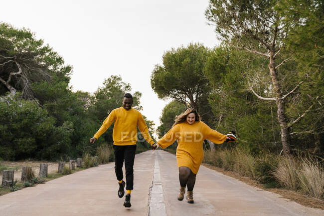 Casal despreocupado de mãos dadas enquanto corre na estrada — Fotografia de Stock