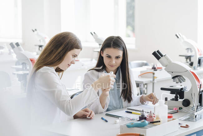 Jeunes chercheuses en blouse blanche examinant un échantillon de laboratoire en classe de sciences — Photo de stock