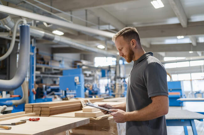 Portrait of carpenter standing in production hall with clipboard in hands — Stock Photo