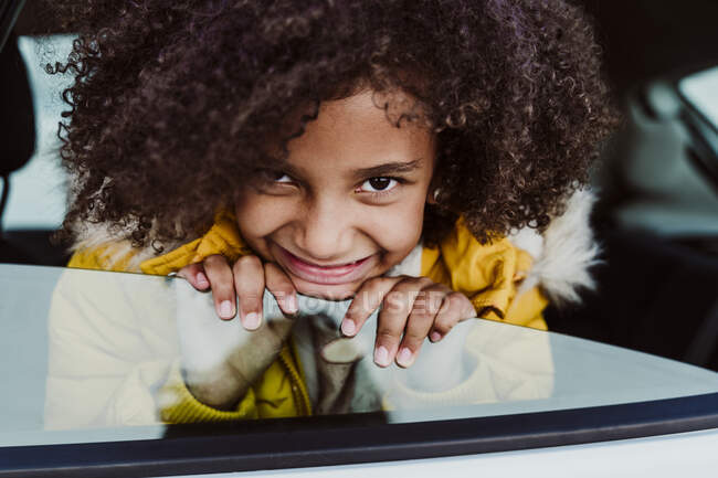 Gros plan de fille souriante avec les cheveux bouclés regardant par la fenêtre de la voiture — Photo de stock