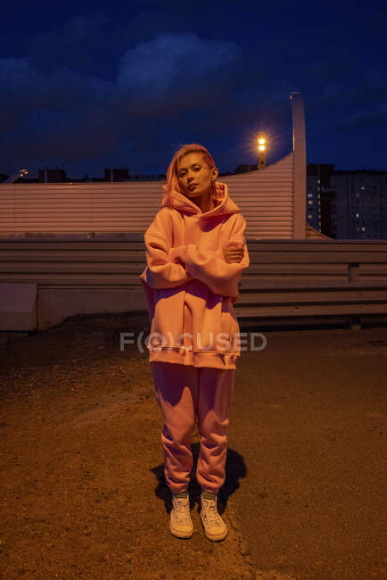 Portrait de jeune femme aux cheveux roses portant un survêtement debout devant le bâtiment la nuit — Photo de stock