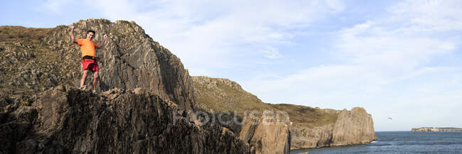 Allegro scalatore di roccia maschio maturo con le braccia sollevate in piedi sulla scogliera — Foto stock