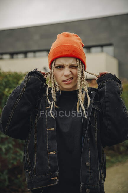 Jeune femme tenant les cheveux tressés clin d'oeil tout en se tenant à l'extérieur — Photo de stock