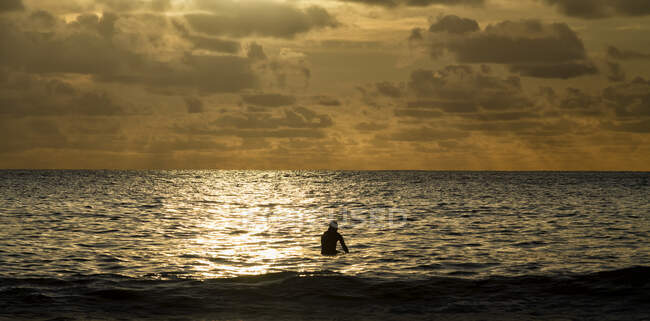 Silhueta do homem no mar durante o pôr do sol em Freshwater West, Pembrokeshire, Reino Unido — Fotografia de Stock