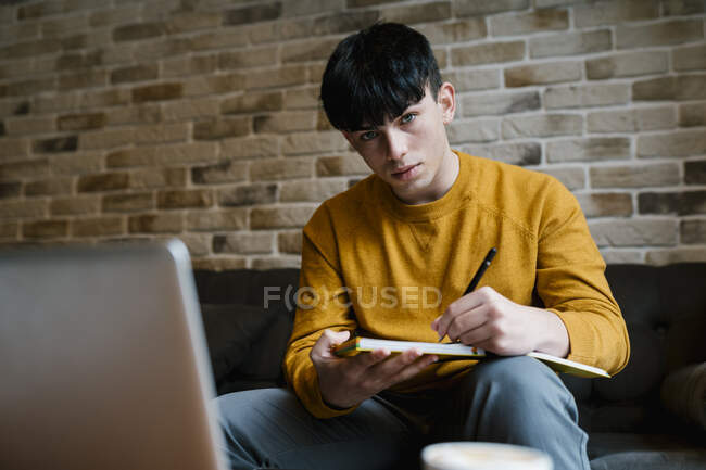 Hombre con portátil y libro mirando mientras está sentado en la cafetería - foto de stock
