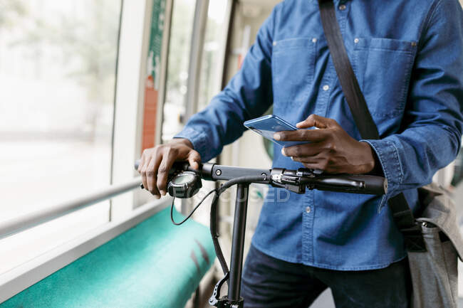 Африканский бизнесмен держит смартфон во время путешествия на электроскутере — стоковое фото