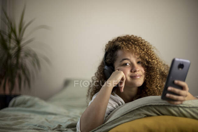 Jeune femme souriante avec téléphone intelligent couché sur le lit dans la chambre — Photo de stock