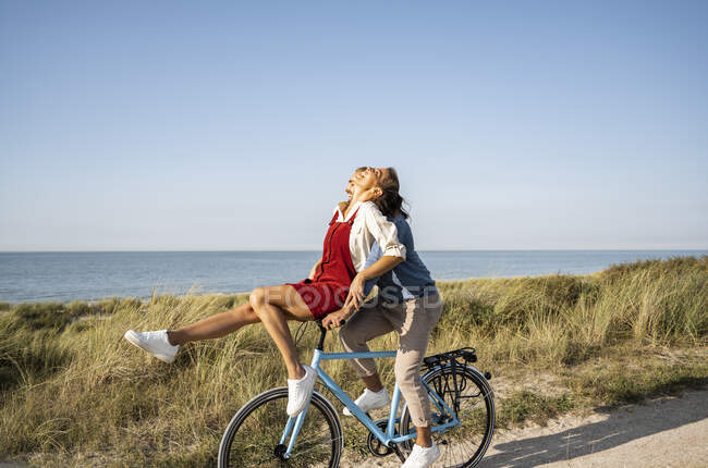 Felice ragazza seduta sulla maniglia mentre godendo giro in bicicletta con il fidanzato contro il cielo limpido — Foto stock