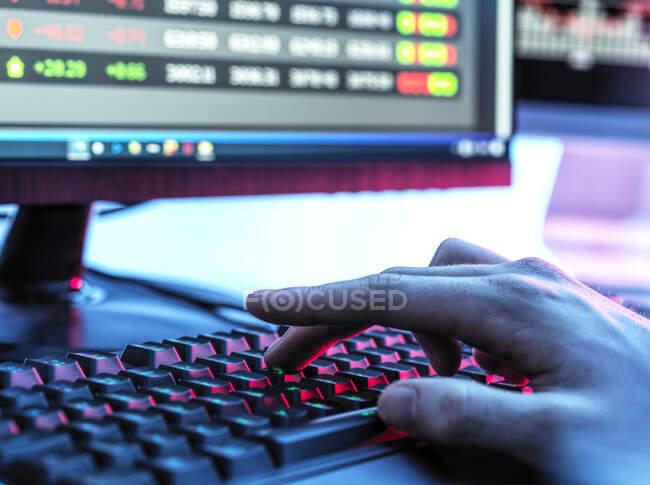 Hands of trader typing on keyboard in front of computer monitor displaying stock market data — Stock Photo