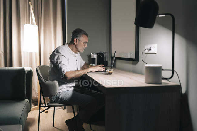 Зрілий чоловік сидить за столом з кавою під час ноутбука в готельному номері. — стокове фото