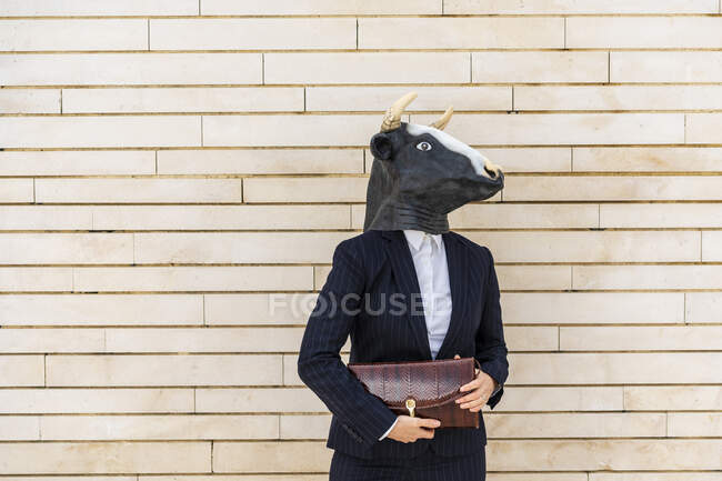 Femme entrepreneur portant un masque de taureau tenant sac à main tout en se tenant par le mur — Photo de stock