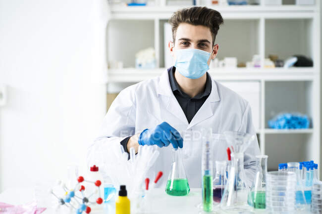 Científico masculino que usa mascarilla protectora mientras trabaja en laboratorio durante pandemia - foto de stock