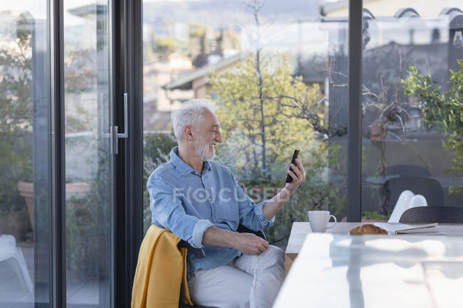 Lächelnder Senior telefoniert zu Hause per Videotelefon — Stockfoto