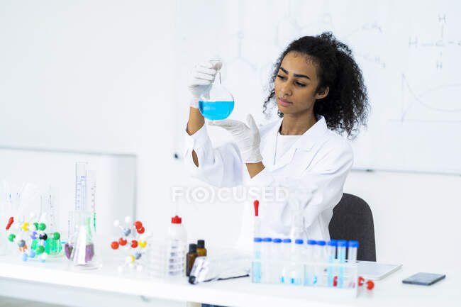 Química joven examinando líquido en frasco en laboratorio - foto de stock