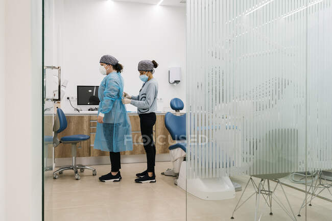 Assistente medico che aiuta a vestirsi in abiti protettivi in clinica durante COVID-19 — Foto stock