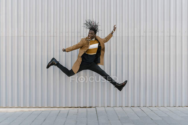 Hombre sobresaliendo lengua mientras salta contra la pared gris - foto de stock