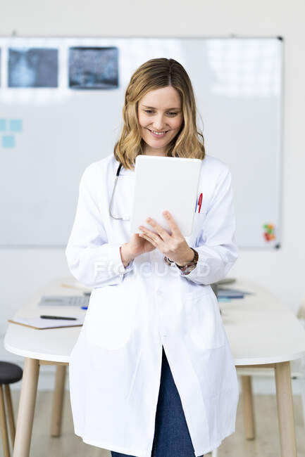 Assistente medico sorridente utilizzando tablet digitale mentre in piedi contro scrivania — Foto stock