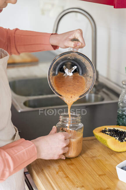 Jeune femme versant smoothie en pot de maçon dans la cuisine à la maison — Photo de stock