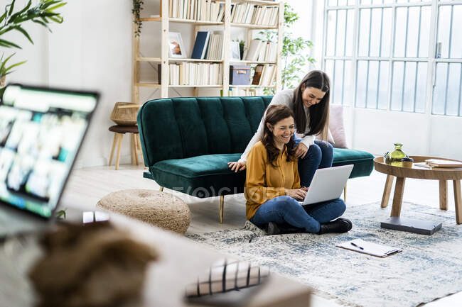Cheerful daughter assisting mother using laptop at home — Stock Photo