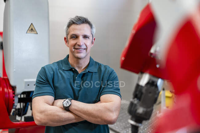 Uomo sorridente con le braccia incrociate in piedi in fabbrica — Foto stock