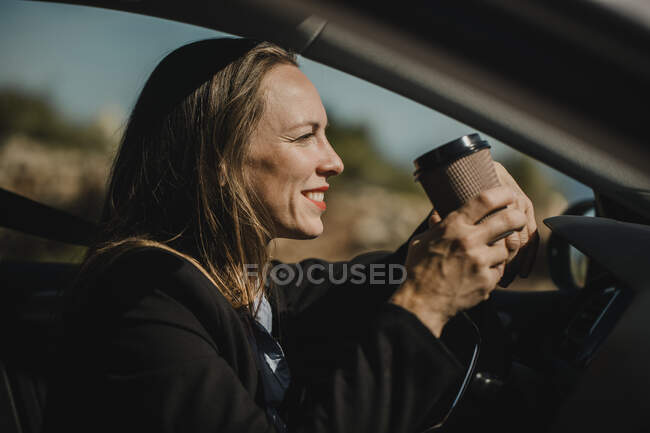 Предприниматель пьет кофе, сидя в машине в солнечный день — стоковое фото