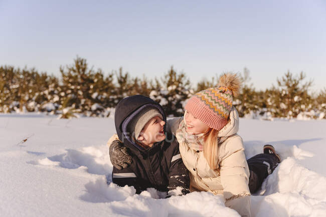 Игривые братья и сёстры зимой лежат на снегу против неба — стоковое фото
