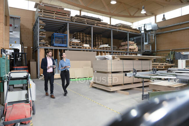 Empresários masculinos e femininos discutindo enquanto caminham no armazém da fábrica — Fotografia de Stock