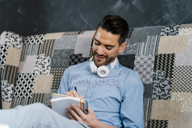 Empresario escribiendo en libro mientras trabaja en casa - foto de stock