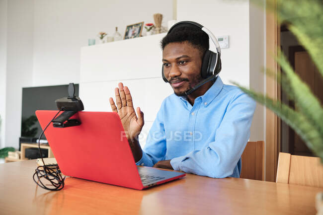 Mid adult businessman with headset waving hand on video call through laptop at home — Stock Photo