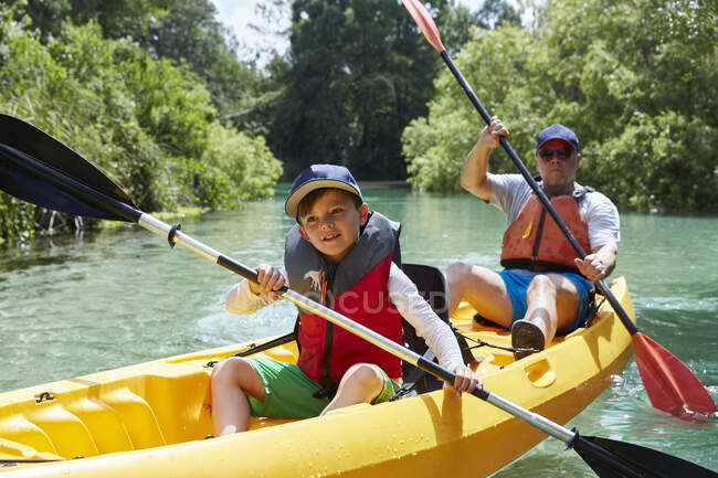 Улыбающийся мальчик смотрит в сторону, катаясь на каноэ с отцом в озере — стоковое фото